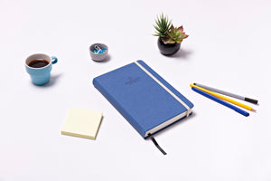 side angle picture of Reboot Habit Journal on a white table, with pens, notepad, and coffee 